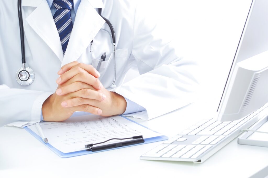 医者がパソコンの前で手を組んでいる画像