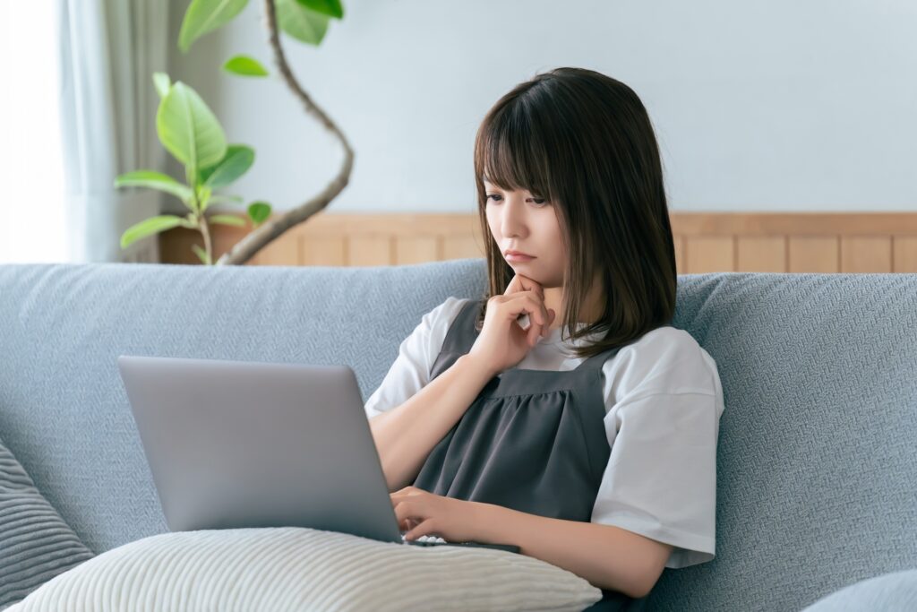 ソファに座ってパソコンを使う女性の画像
