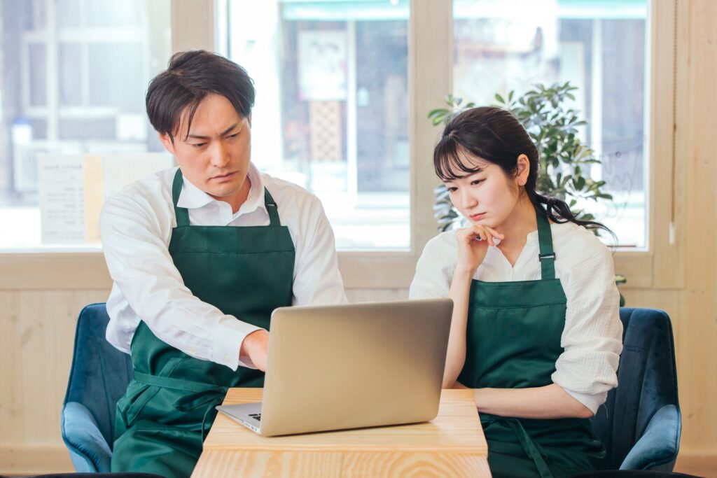 パソコンの前で悩むカフェ店員の画像