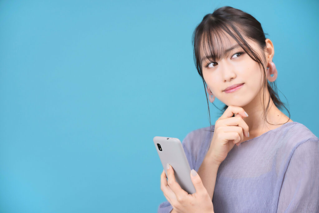 スマホを持ち考える女性の画像