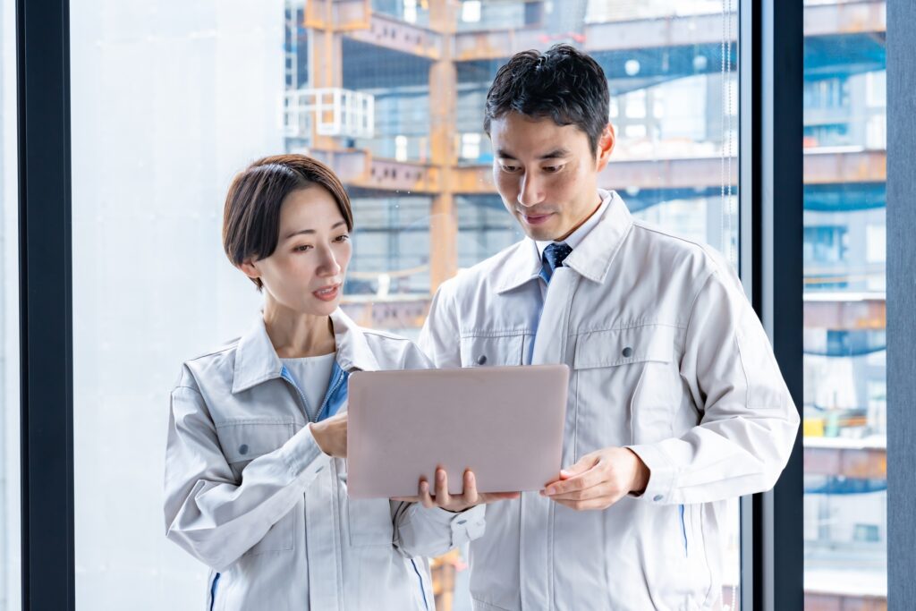 ビルでパソコンを見る作業着を着た男女の画像