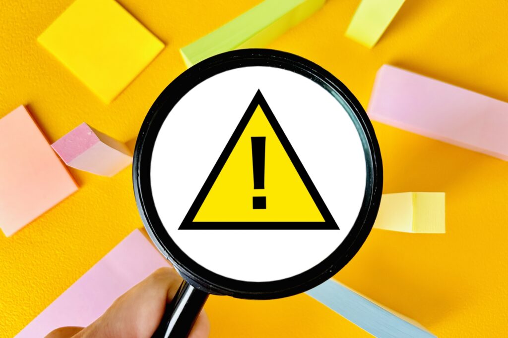 虫眼鏡を持つ手と注意マークの画像