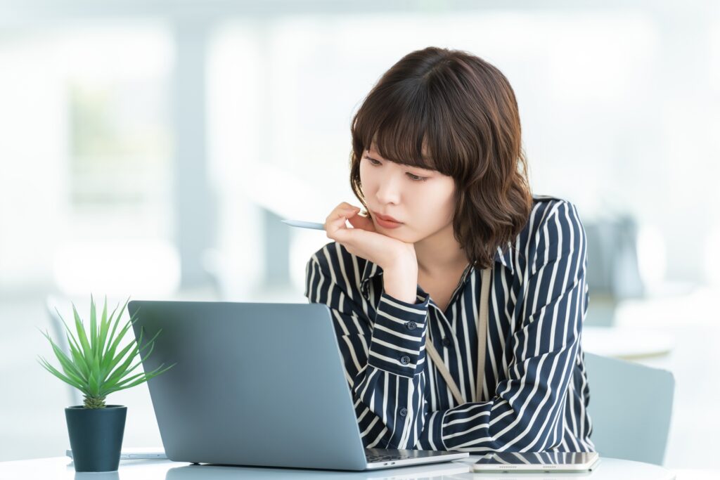 パソコンを使いながら考える女性の画像