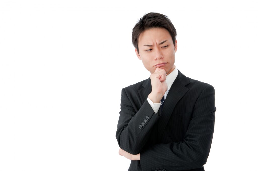 あごに手をおいて考える若いビジネスマンの画像