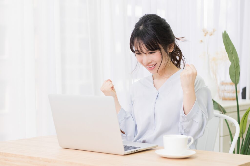 パソコンの前でガッツポーズをする女性の画像